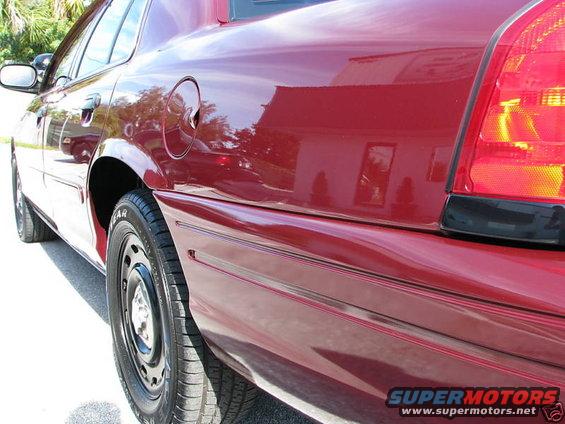 Red 2005 Ford Crown Victoria, rear quarter panel, side view. Black steel wheels, chrome fuel door. Minor dent on rear quarter panel