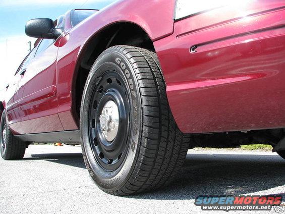 Close-up side view of a red sedan's front wheel and fender. The tire is a Goodyear. The wheel is a black steel rim with a chrome hubcap