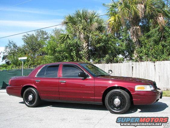 Red 2005 Ford Crown Victoria sedan, side view, black steel wheels, tinted windows, minor dirt on body