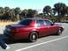 2005 Ford Crown Victoria - A red Ford Crown Victoria is parked in a lot with palm trees in the background under a clear sky.