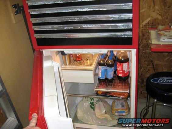 Red refrigerator with drinks and a toolbox above