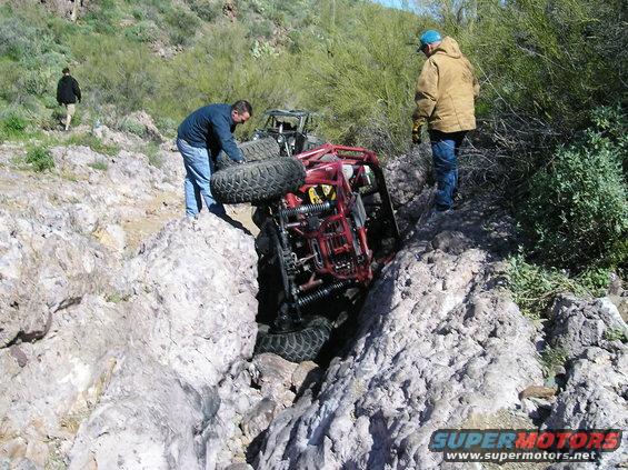 Red off-road buggy stuck in rocky terrain with two people nearby