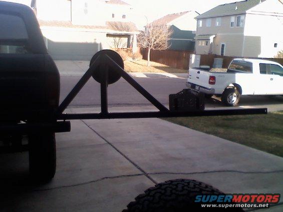 Rear tire carrier on dark SUV, with a white pickup truck in the background
