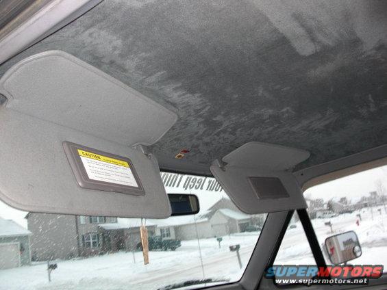 Interior shot of a truck's headliner and sun visors. Snow is visible outside the windshield