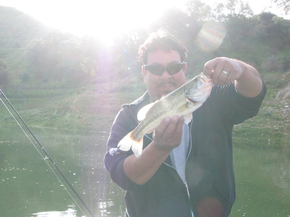 Man in sunglasses holds a bass while fishing on a lake
