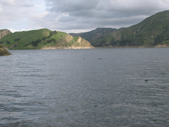 Lake with choppy water and green hills under a cloudy sky