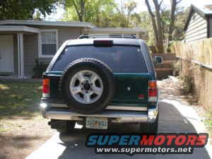 Rear view of a green SUV parked in a driveway. It has a spare tire mounted on the back
