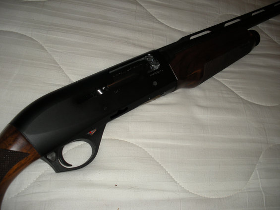 Close-up of a black shotgun with wood stock, resting on a white, quilted surface