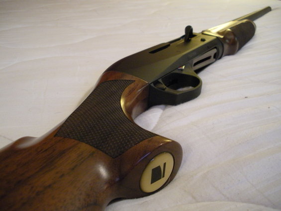 Shotgun stock with wood grain and textured grip, close-up on a white surface