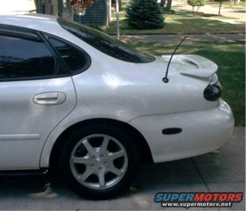 Rear quarter panel and trunk of a white sedan with a spoiler and antenna. Watermark says SUPERMOTORS