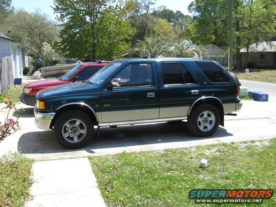 Green and tan SUV parked next to a red car. The SUV has a spare tire cover on the back