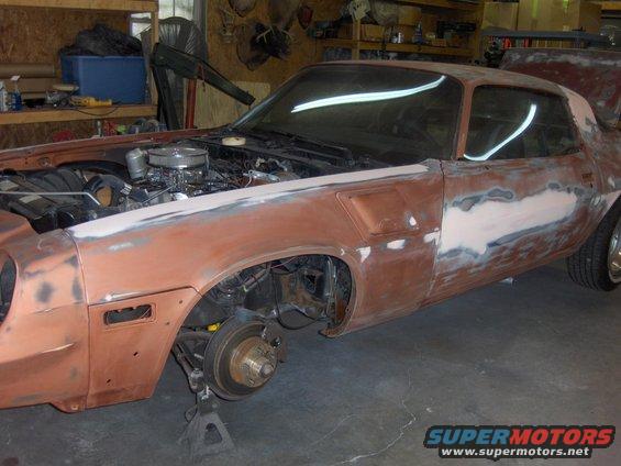 Car bodywork in progress, engine exposed, front wheel off, on jack stands