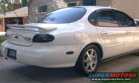 White sedan parked in driveway, rear quarter view. License plate reads 'SOE 86'