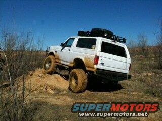 White 1992 Ford Bronco climbing a dirt hill with a roof rack and spare tire