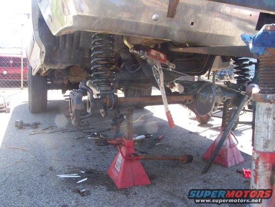 Vehicle rear axle removed and supported by jack stands, with suspension components visible