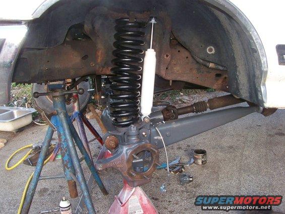 close-up of a vehicle's front suspension and axle assembly, with a new shock and coil spring installed, supported by jack stands