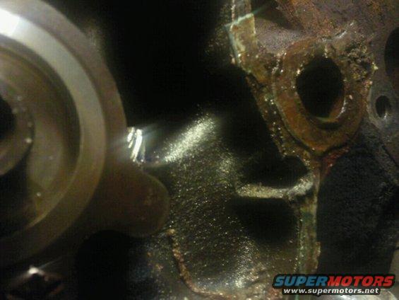 Close-up of a damaged engine block with oil residue and a circular metal component