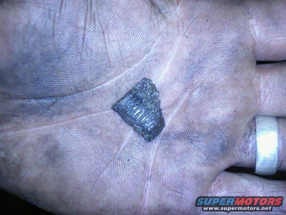 Hand holding a broken piece of an engine block with visible internal metal structure. A ring is on one finger