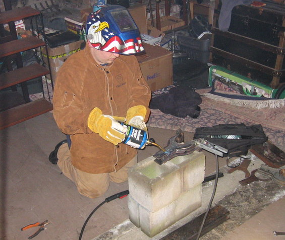Person in welding mask and protective gear welding metal on cinder blocks