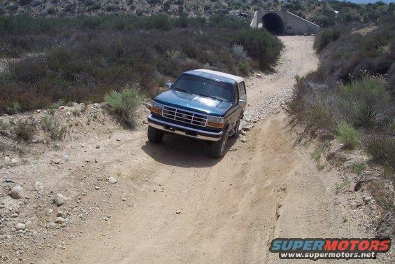 Teal Ford Bronco driving on a dirt road