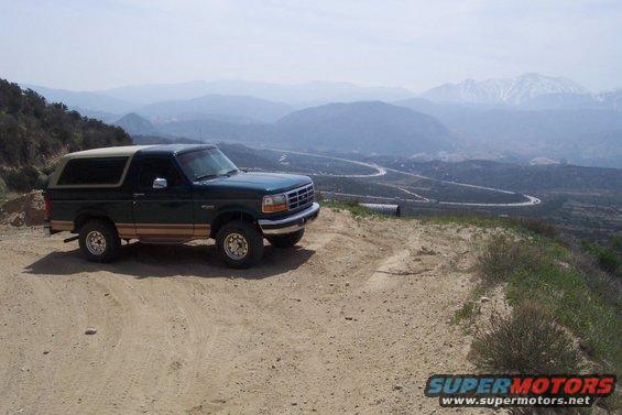 Green 1995 Ford Bronco parked on a dirt overlook, tan trim, mountains in background