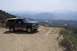 1995 Ford Bronco - A green 1995 Ford Bronco with tan trim sits on a dirt road, offering a view of a winding road and distant mountains.