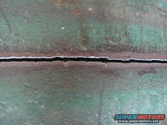 Close-up of a cracked metal surface with green and brown patina. Supermotors.net logo visible