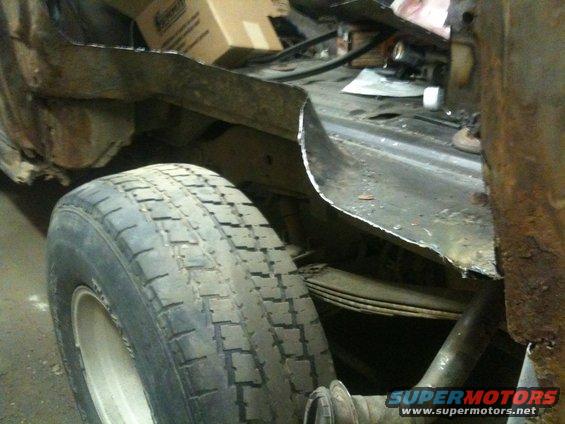 Rear tire and suspension components of a vehicle, with significant rust and body damage visible