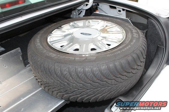 Spare tire with Ford-branded hubcap in car trunk