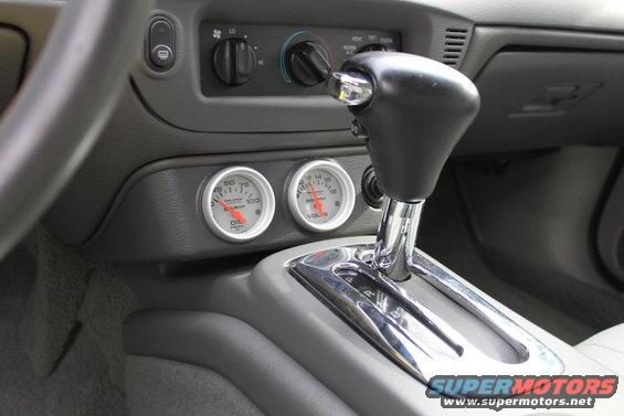 Car interior showing gear shifter, climate controls, and two aftermarket gauges (oil pressure and voltage)