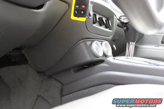 Car interior showing dashboard, gear shifter, and two gauges. Gray carpet and upholstery visible
