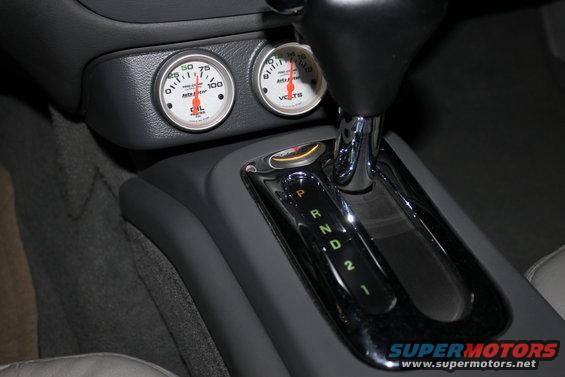 Car interior showing two gauges and a chrome-trimmed automatic gear shifter with illuminated P, R, N, D, 2, 1 indicators