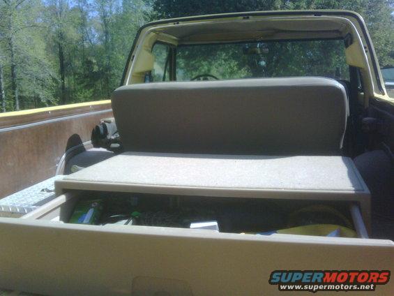 Yellow 1978 Ford Bronco interior rear cargo area with folded-down rear seat and storage drawer