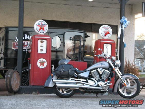 Silver motorcycle parked at vintage Texaco gas station with old truck in background