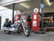 2006 Victory Kingpin - A silver motorcycle is parked at a vintage gas station, with two red gas pumps and a classic car visible behind it.