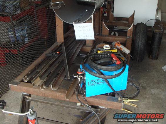 Welding equipment and metal stock on a workbench, with a tire visible in the background