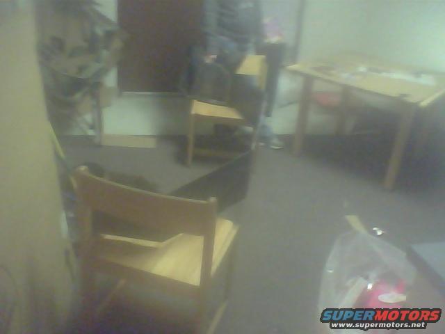 Interior shot of a room with a wooden chair in the foreground and a table in the background. A watermark reads SUPERMOTORS