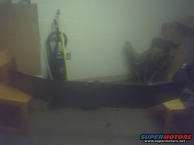 Black car bumper, possibly from a truck, lying on the floor indoors