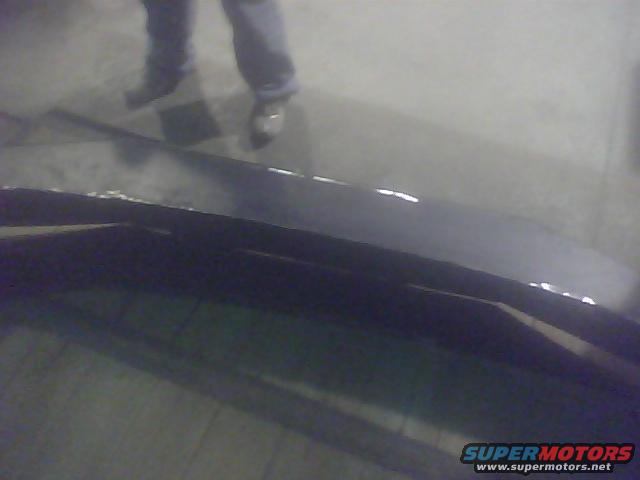 Dark colored truck bed with visible reflections and a person's legs standing above