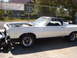 1973 Ford Ranchero - A white coupe utility with its hood open is parked outside next to a chain-link fence.
