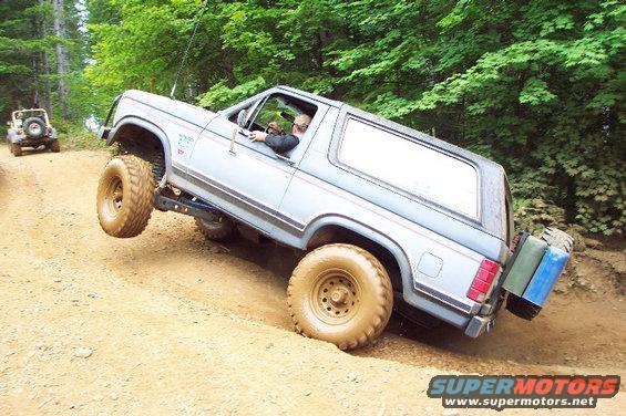 Ford Bronco climbing a dirt hill with one wheel off the ground. Another Jeep is behind it