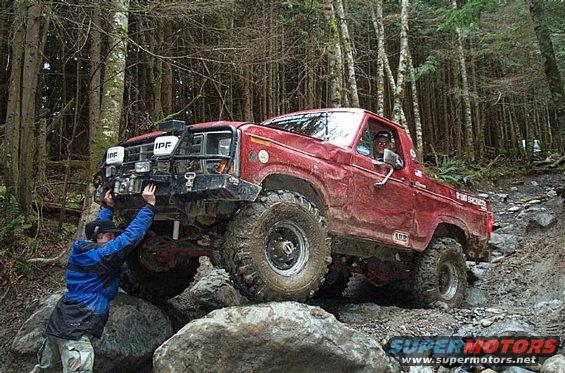 Red pickup truck with off-road modifications, being pushed by a person on a rocky trail