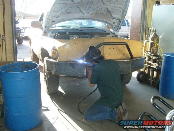 Man welding a custom bumper onto the front of a 2000 Dodge 1500 truck