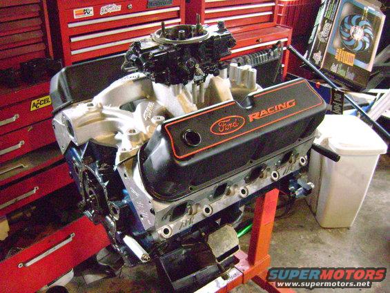 Ford V8 engine with black racing valve covers and orange trim, mounted on an orange engine stand
