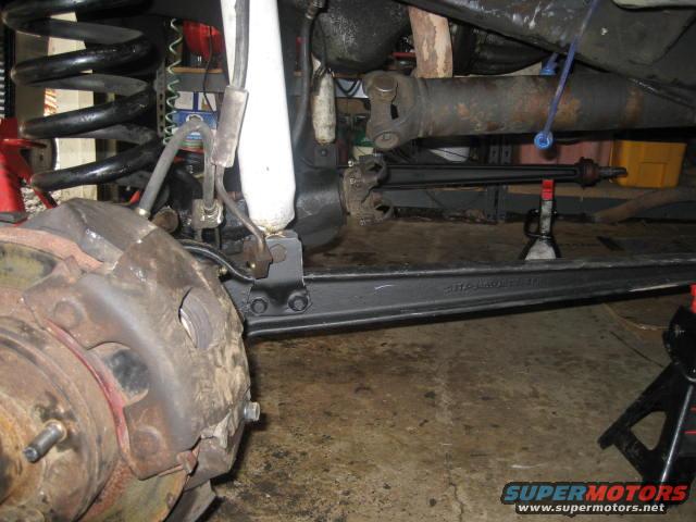 Close-up of vehicle's front brake caliper, suspension spring, shock absorber, and driveshaft
