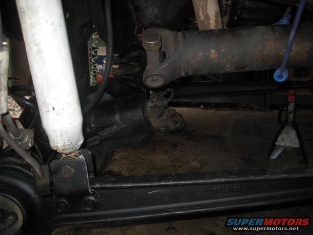 Close-up of a vehicle's rear axle, driveshaft, and shock absorber, with the vehicle supported by jack stands