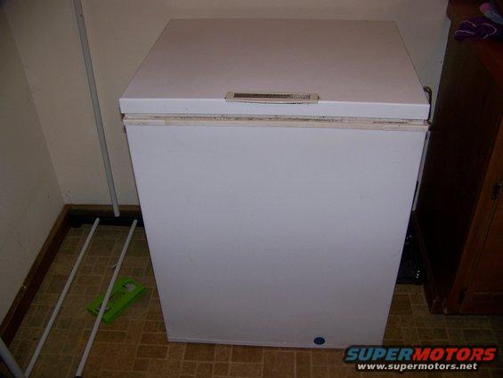 White chest freezer in a room with tiled floor and wooden cabinet