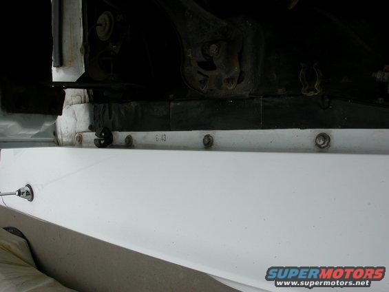 Close-up of a white car part with 'G.43' stamped on it, showing bolts and suspension components above