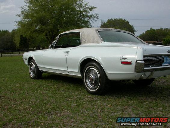 White 1968 Mercury Cougar parked on grass, showing rear quarter panel and grille. Vinyl top visible
