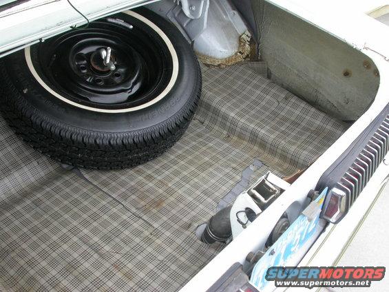 Trunk interior of a 1968 Mercury Cougar with a plaid liner and a spare tire
